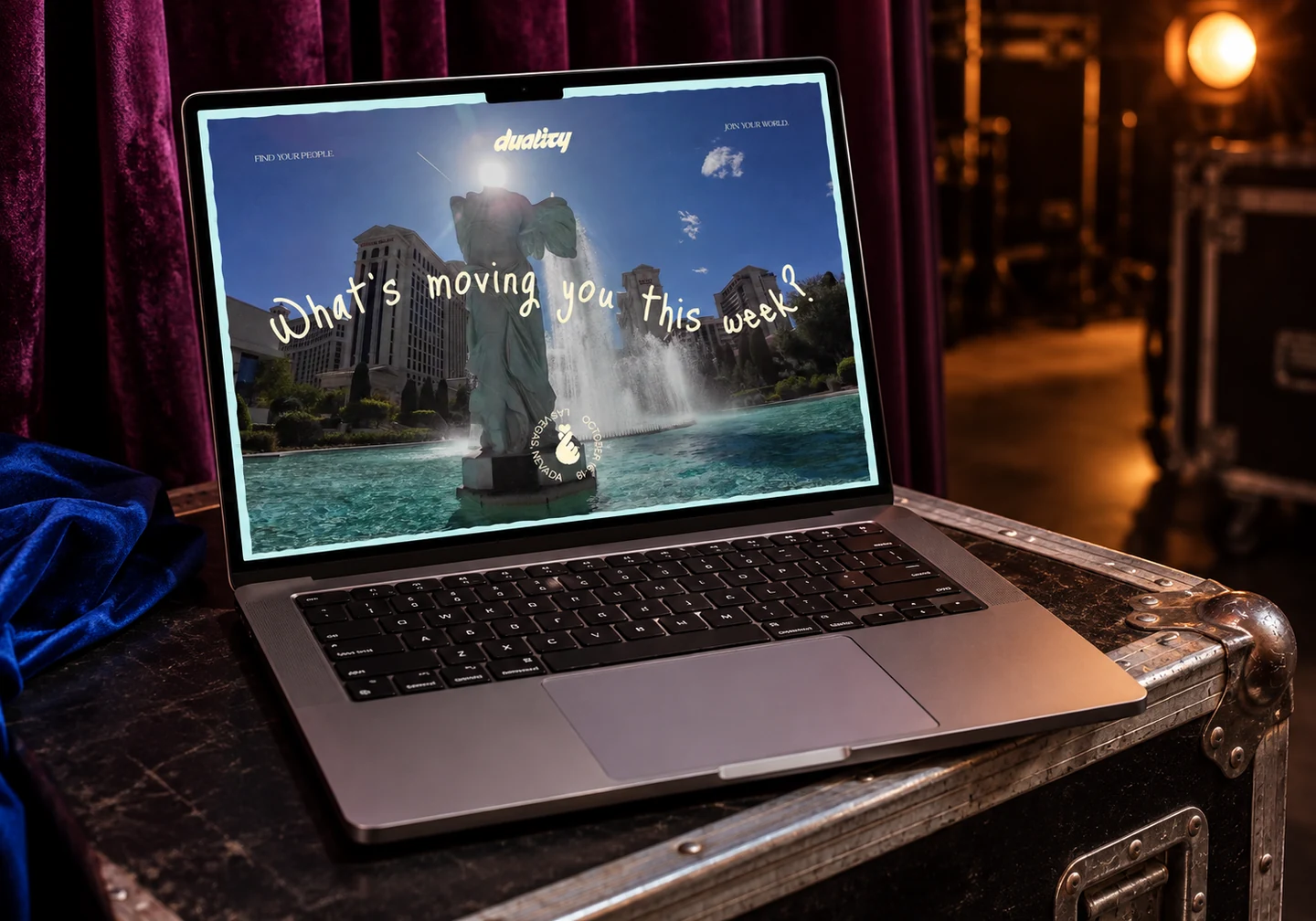 Duality homepage on a MacBook on a backstage flight case beside velvet curtains.