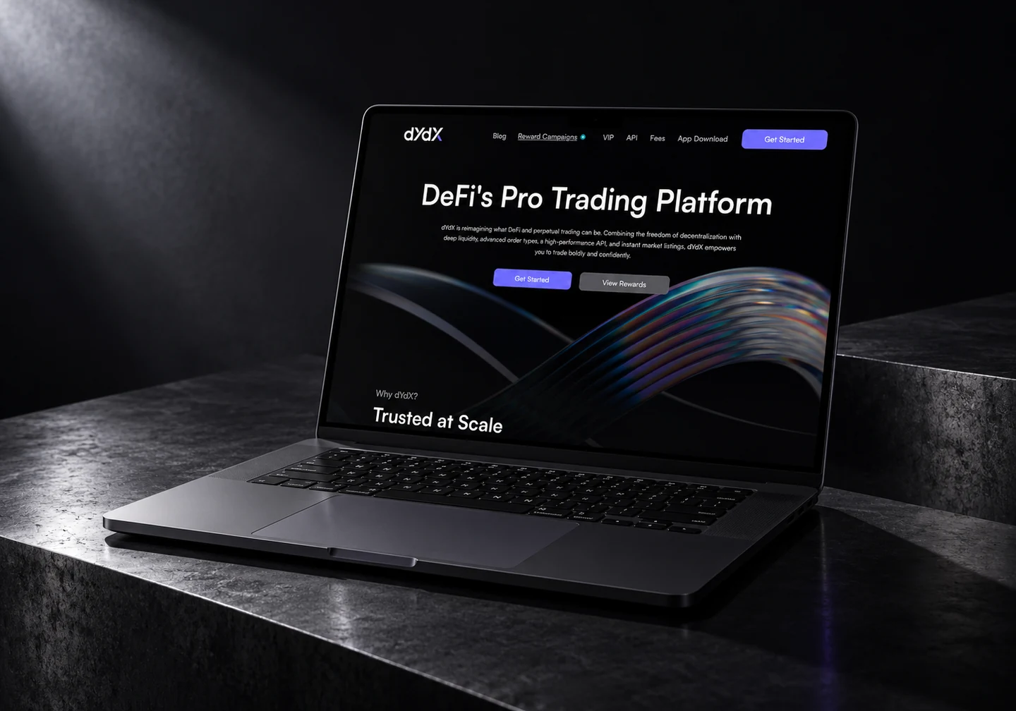 dYdX homepage on a dark MacBook on blackened steel under directional light.
