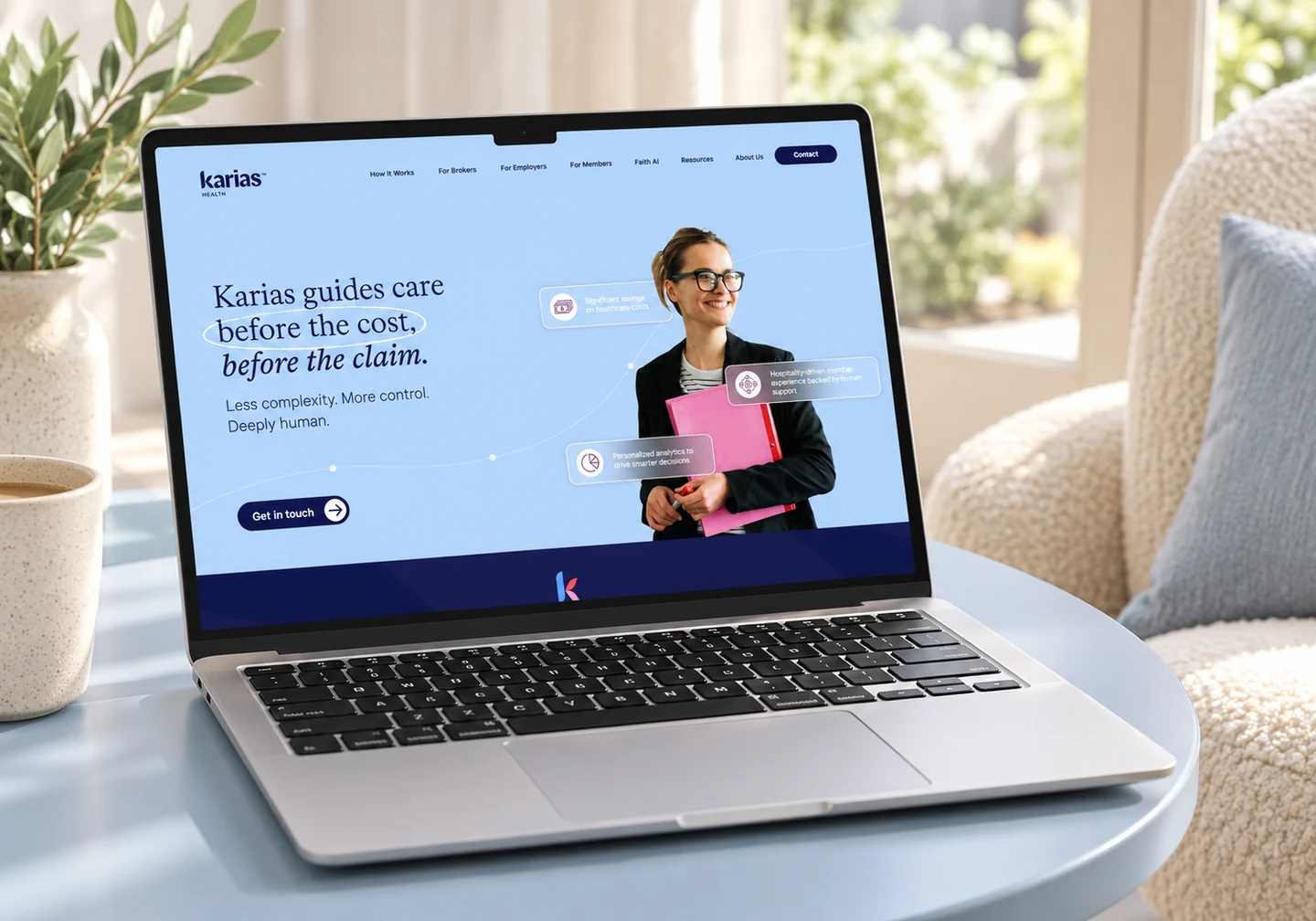 Karias Health homepage on a silver MacBook in a calm blue and cream lounge.