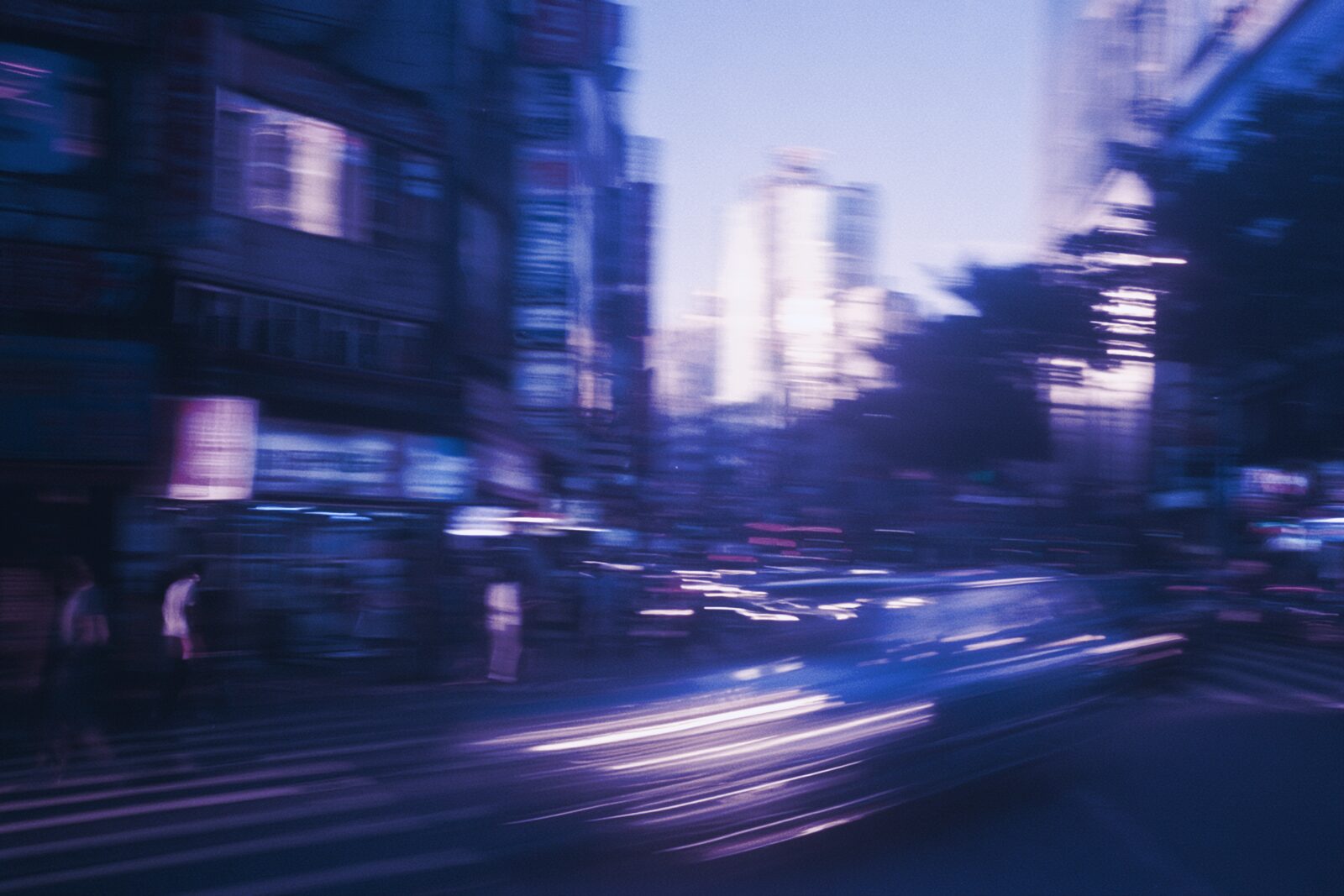 A busy city street at night, storefronts sharp while traffic blurs past