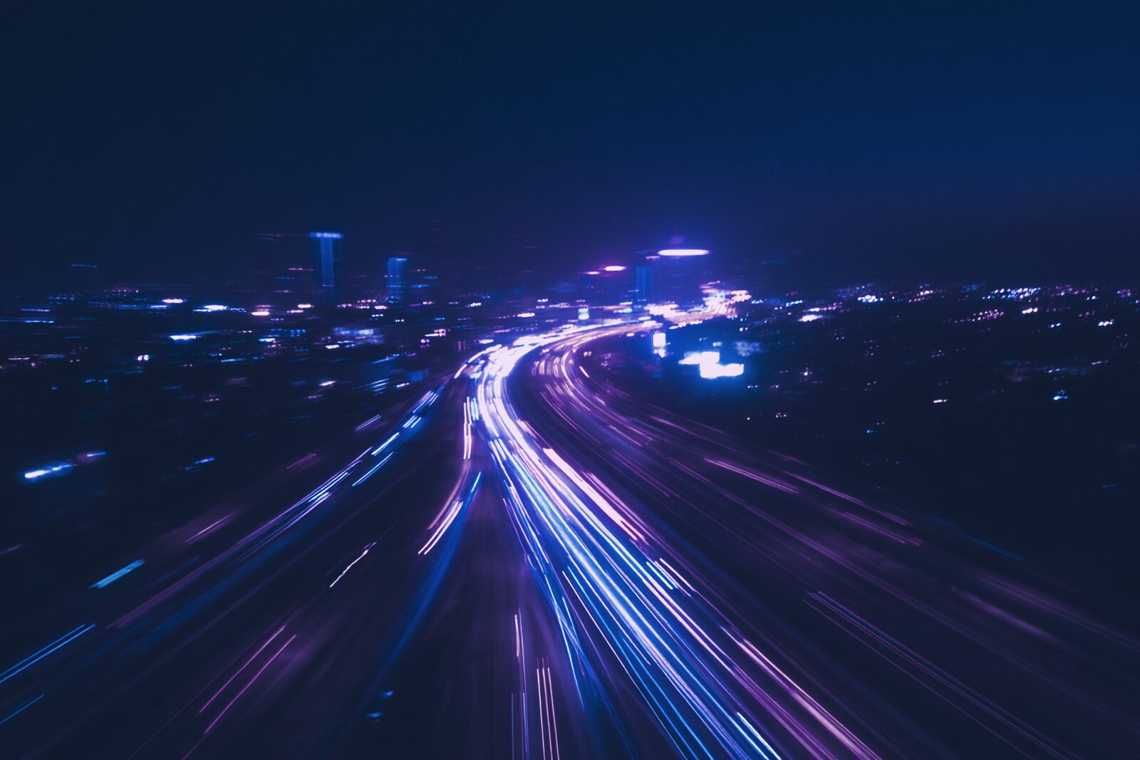 Aerial long exposure of a night road interchange, traffic reduced to streams of light