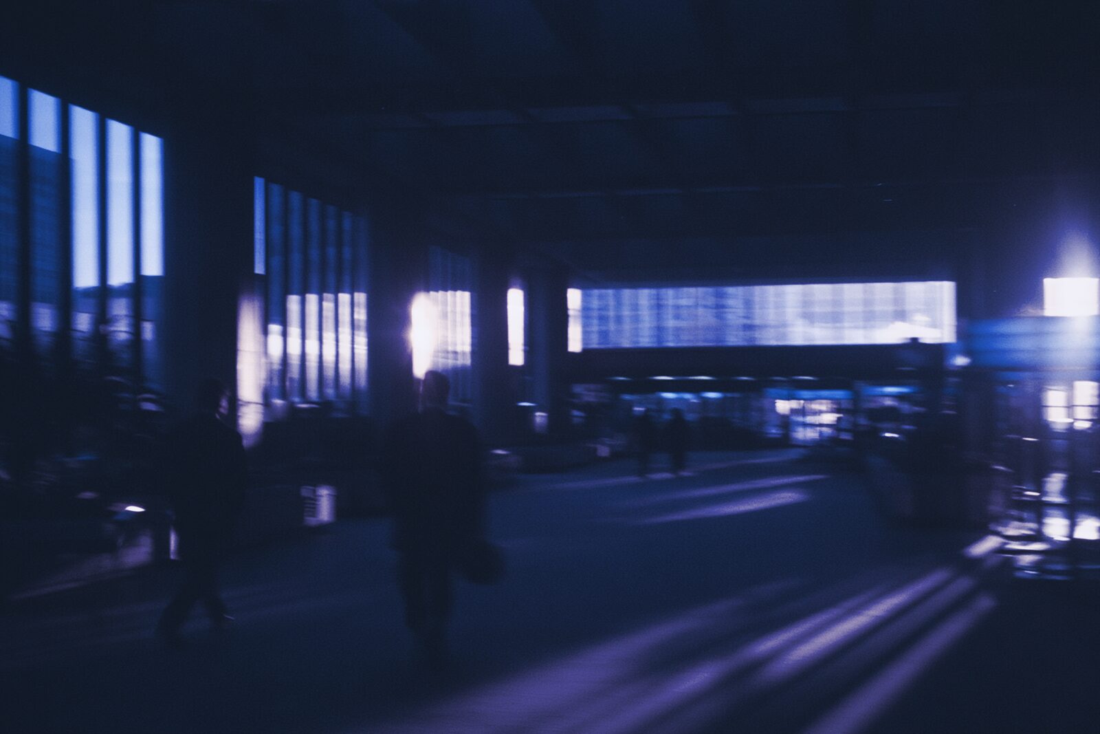 Two figures walking away down a wide concourse, the architecture sharp around them